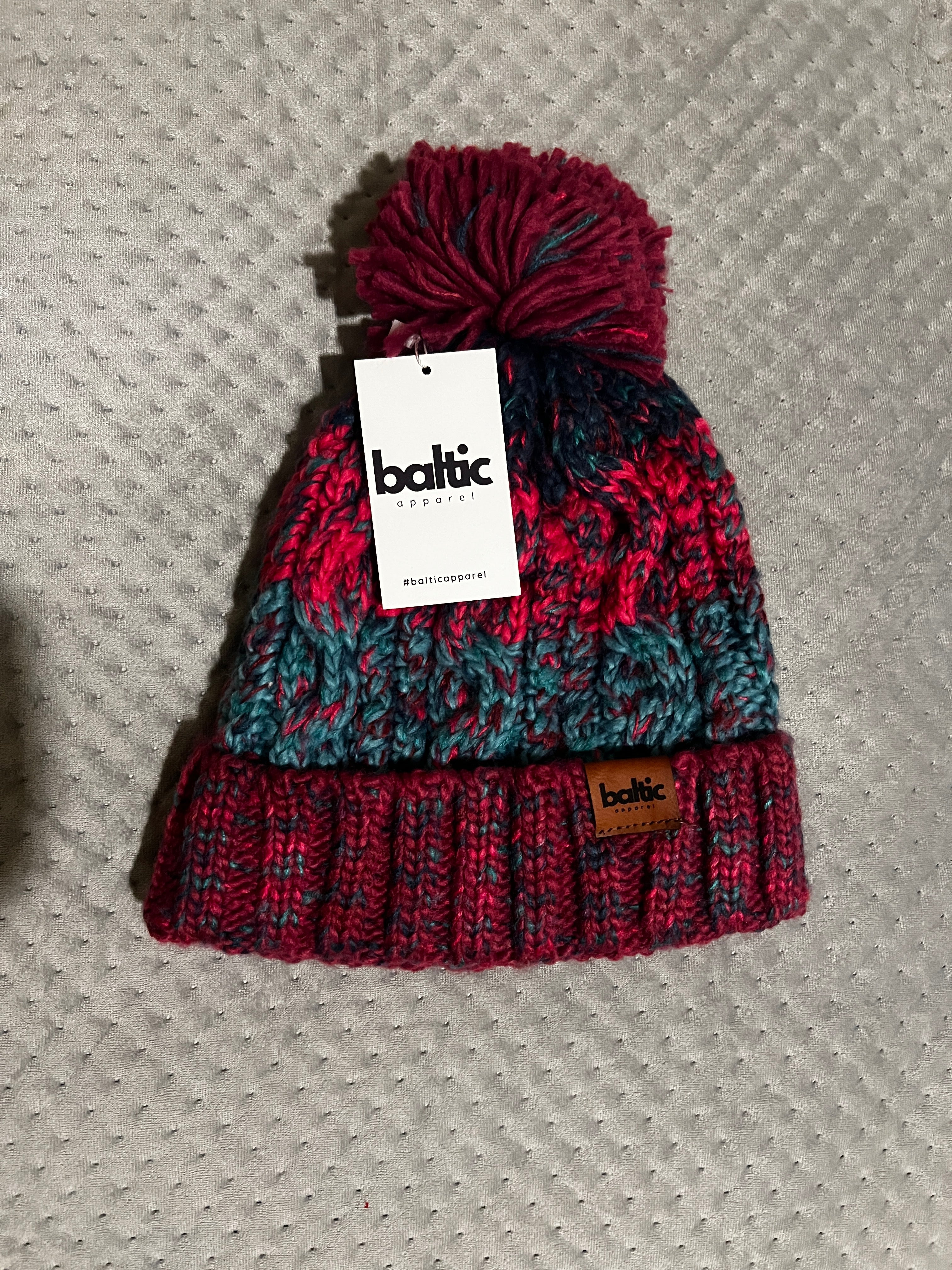 Knitted beanie with pom-pom and 'baltic' tag on a textured surface