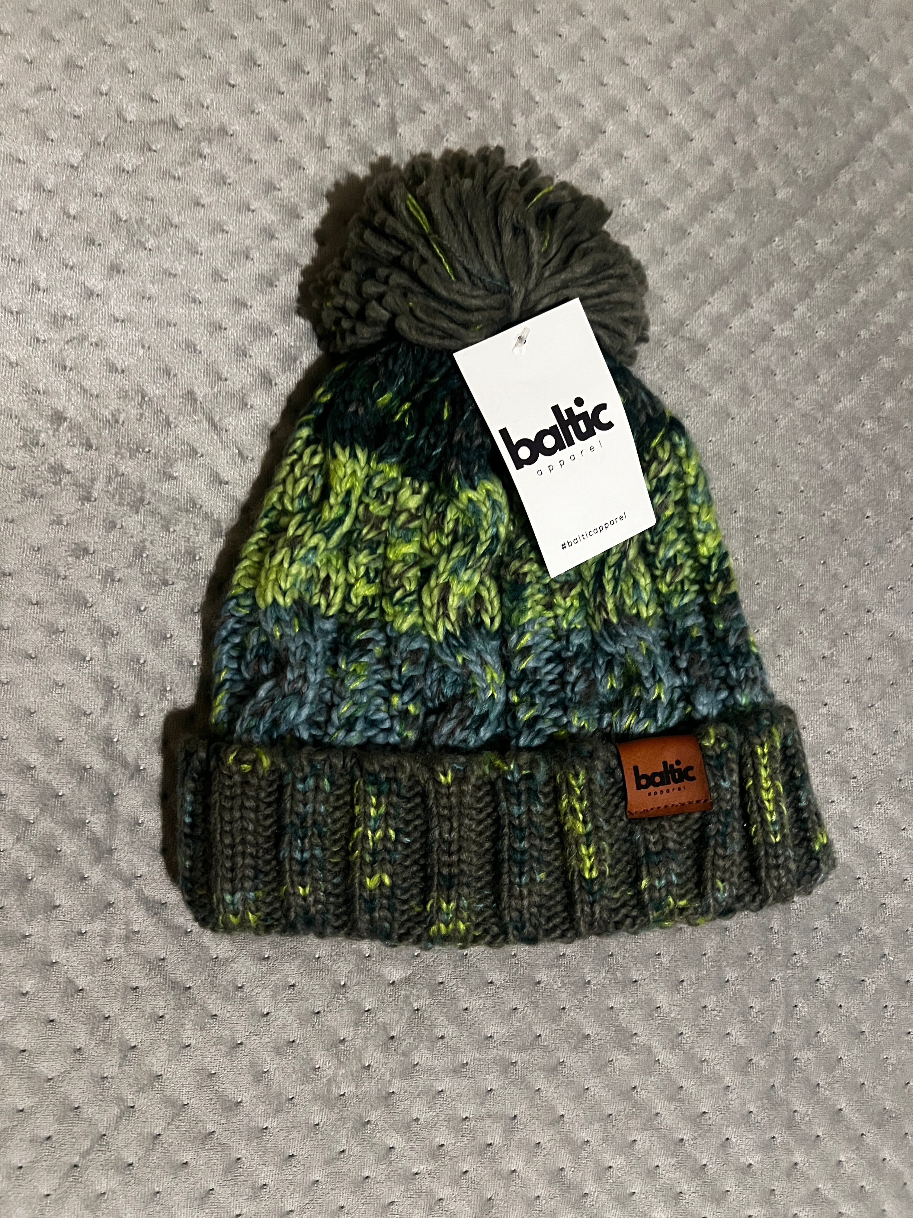 Knitted beanie with pom-pom and brand tag on a textured surface